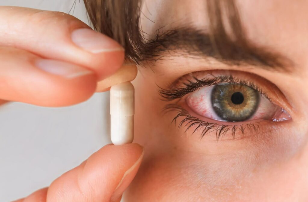 Close-up of a person holding a supplement next to their red, dry eye.