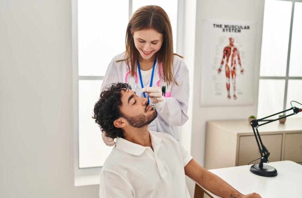 An optometrist uses an eye dropper to squeeze medicated eye drops into their patient's dry eyes.