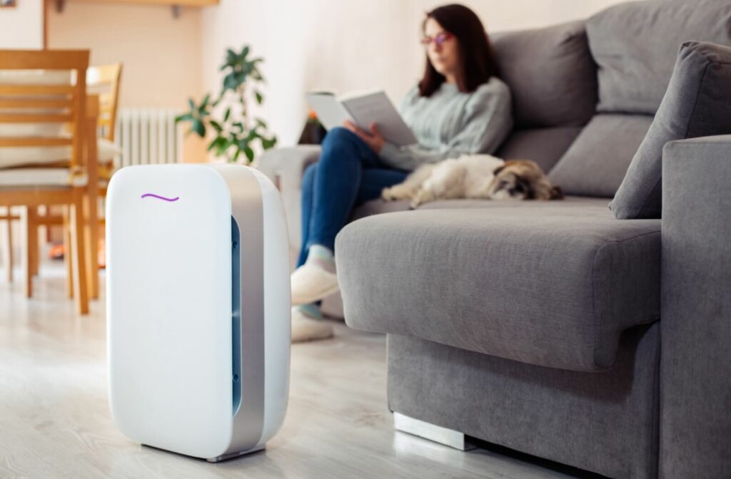 A person sitting on their couch reading a book with their air purifier running in the livingroom.