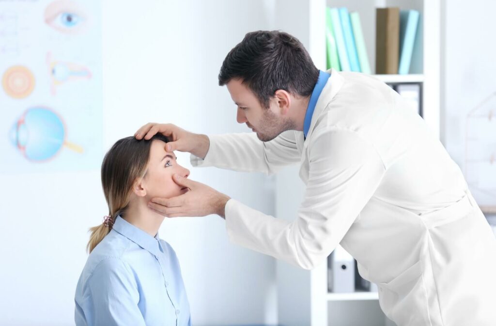 A person sits in a clinic while an eye care professional gently examines their eye using both hands.