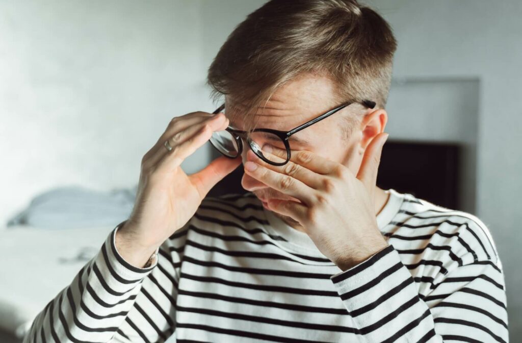 A person, wearing a striped shirt and glasses, rubbing their eyes due to dry eye symptoms.