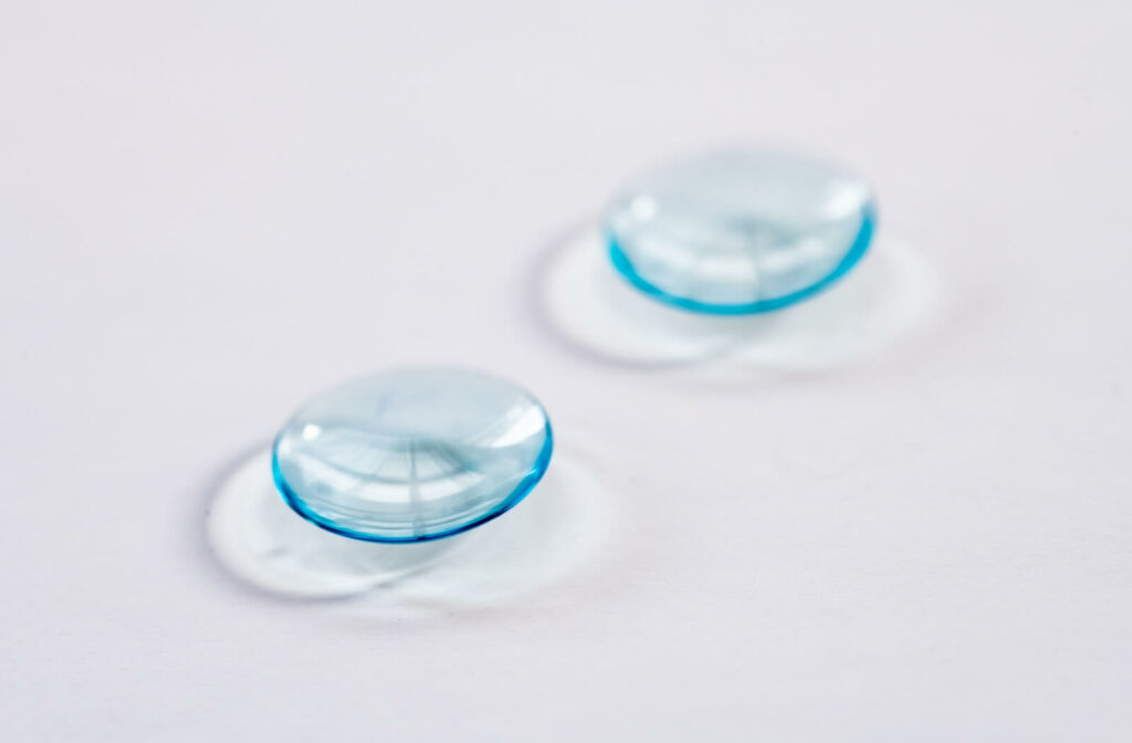 Two soft blue-tinted multifocal contact lenses resting on a white surface, showing their curved design and light reflections.
