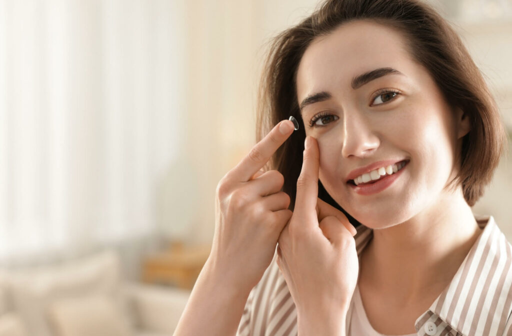 Smiling person holding a contact lens on the fingertip, preparing to apply it to the eye.