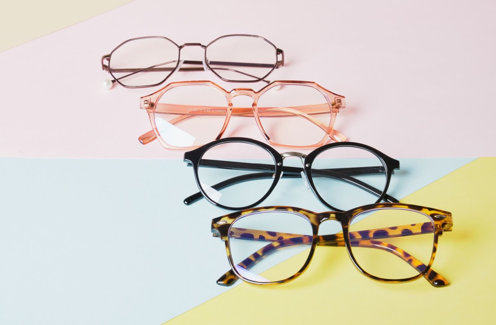 Four pairs of stylish eyeglasses in different colors and shapes arranged on a colorful pastel background.